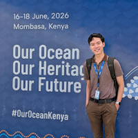 A photo of Chief Impact Officer Mitchelle De Leon standing in front of a large blue sign at the conference. Text on the sign, to his right, reads: 16-18 June, 2026, Mombasa, Kenya, Our Ocean, Our Heritage, Our Future, #OurOceanKenya. 