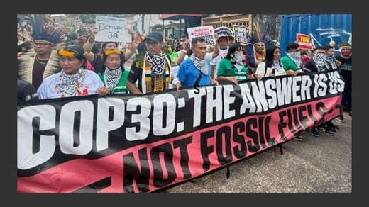 A photo of a group of people on a city street holding a banner that reads: COP30: The answer is us - not fossil fuels